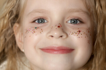 Portrait of cute little blonde girl with blue eyes and glitters on her face.