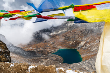 View of Lake Angladumba Tsho, snow capped mountains of the Himalayas, desert valley and Buddhist prayer flags during EBC trekking. View from Renjo La pass, Solukhumbu, Sagarmatha, Nepal.
