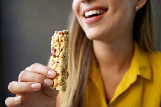Unidentified girl eating an energetic nuts cereal bar on gray background