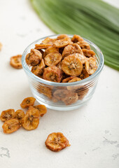 Dried fresh organic banana slices in glass bowl with green leaf.