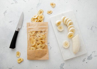 Pack of dried healthy bio banana chips with knife and raw banana.
