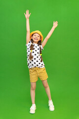 A full-length teenage girl dressed in a summer hat and shorts. A beautiful little lady has raised her arms and is reaching up. Summer clothes for recreation. Green isolated background.