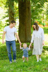 Fototapeta premium Happy family, dad, mom, child walk together in a park in nature, holding hands. Concept of family vacation, first steps.