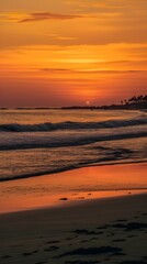 Vertical shot of a beach with the sun setting over the horizon, reflecting off of the tranquil water