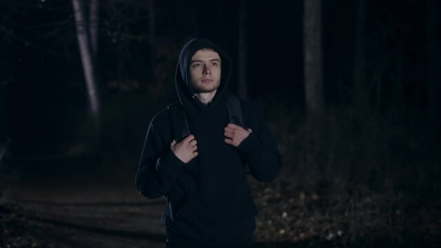 A young guy returns home through the forest. A man with a backpack walks through a dark night forest.