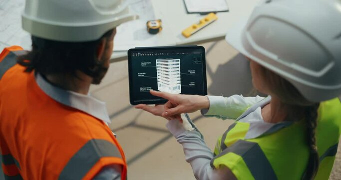 Site Manager Talking with General Construction Operative at a Residential Building Construction Area. Female and Male Employees Using a Tablet Computer with a Detailed 3D Building Model