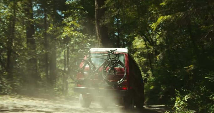 Back shot  of a Westfalia van with a bicycle on back driving on a dirt road with trees in the forest
