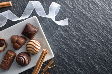 Chocolate bonbons on white plate with ribbon on slate