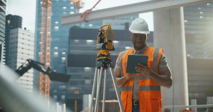Skilled African Worker in High Visibility Vest and a Hard Hat is Designing a Building Site Layout with a Total Station Theodolite. Handsome Civil Engineer Working in Construction Industry