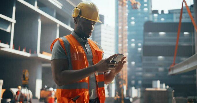 Cheerful Young Black Man Using Smartphone at Work. Civil Engineer Browsing Internet, Sending Text Messages to Friends and Family and Spending Time Online in Entertainment and Social Apps