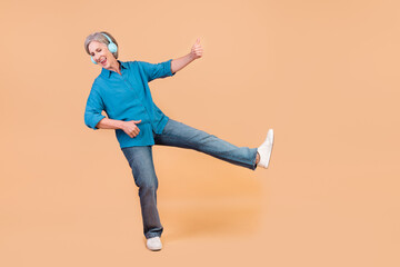 Fototapeta na wymiar Full length photo of carefree ecstatic person wear blue shirt jeans dancing in headphones play guitar isolated on beige color background