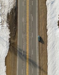 Aerial view of a car driving along a road through a snowy winter landscape