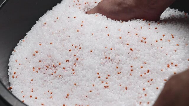 A woman mixes plastic granules with orange pigment to create colored plastic. Polymer composites are used in industry as raw materials for the production of various products