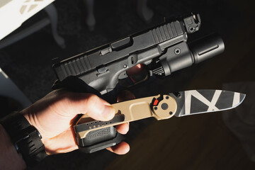 Tactical weapon, G19 pistol with a flashlight and a folding knife in a man’s hand.