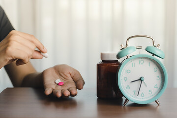 Person holding a pill with a medicine bottle and an alarm clock for time management, deadlines, and...