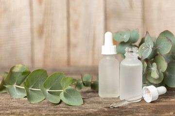 Obraz na płótnie Canvas Eucalyptus essential oil in a glass bottle with green eucalyptus leaves on a textured wooden background. Aromatherapy concept. Spa. Natural organic ingredients for cosmetics and body care.Copy space