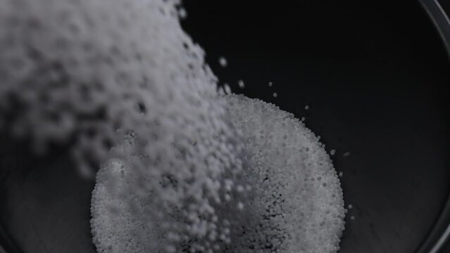 Filling the tank with plastic granules. The process of producing parts from polyethylene compound. White granules are poured into a container.