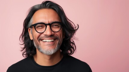 Smiling man with long dark hair and glasses wearing a black shirt against a pink background.