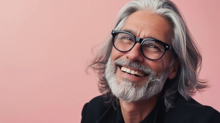 Smiling man with gray beard and hair wearing black glasses against pink background.