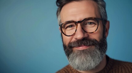 Fototapeta premium A man with a gray beard and mustache wearing glasses smiling against a blue background.