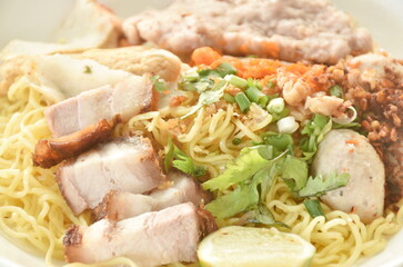 dry Chinese egg yellow noodles topping grilled crispy and boiled chop pork with pork ball dressing cayenne pepper on plate