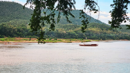 A serene view of the Nam Khan River in Laos, with traditional boats against a backdrop of verdant...