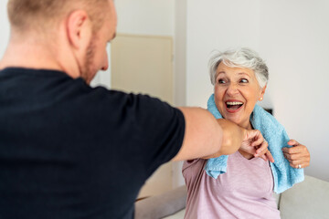 Cropped shot of a young man and old woman bumping elbows. Senior women and fitness trainer exercising together at home.