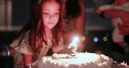 Little girl blowing candle on birthday cake celebrating three years of age