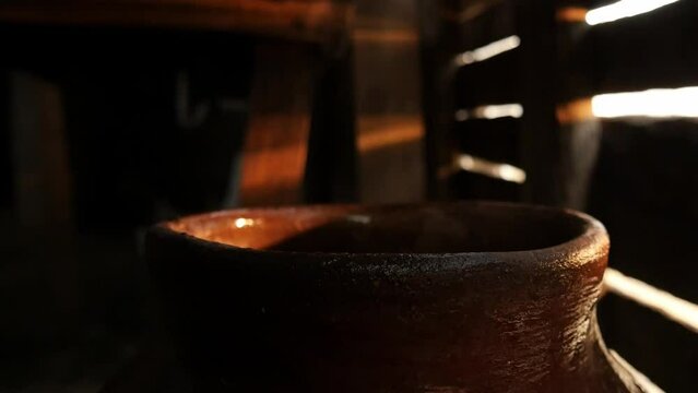 hands of elderly Latino man taking water from a clay container called tinaja with an aluminum glass inside a wooden house in a rural area