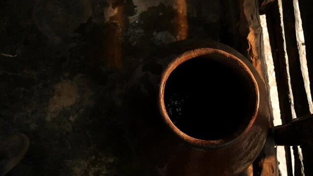 hands of elderly Latino man taking water from a clay container called tinaja with an aluminum glass inside a wooden house in a rural area