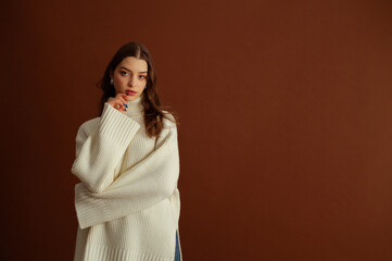 Fashionable confident brunette woman wearing oversized white knitted turtleneck sweater, posing on...