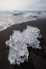 Ocean waves lapping up chunks of ice sparkling in the sun on a black sand beach. Natural wonder,...