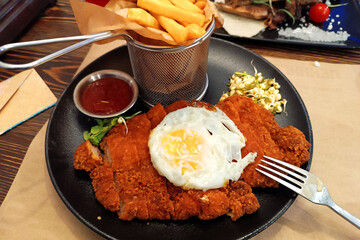 Breaded chicken schnitzel with fried eggs and French fries, served with ketchup