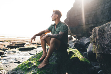 Stylish young guy in green shirt sitting on rock