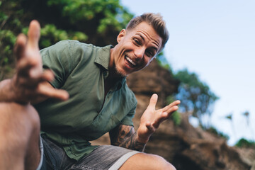 Young excited man showing surprised hands while sitting in nature