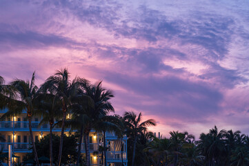 A purple, tropical sunrise in the Florida Keys.  The sky is gettign light and a tropical style building can be seen amoungst the palm trees