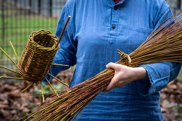 Craftswoman holds woven bird house and sheaf of willow branches, weaving willow basket