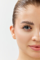 Obraz premium Half-faced portrait of beautiful young woman with clear face, long lashes and laminated eyebrows against white studio background. Concept of beauty, skincare, cosmetics and cosmetology