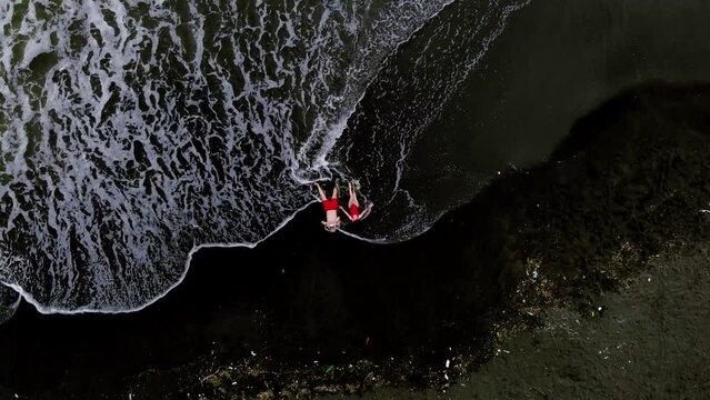 Black sand beach. Fantastic landscape of black sand volcano Ureki beach in Georgia. Couple having a good time on vacation. A man and a woman in red swimsuits are lying down. Garbage after the storm