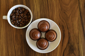 Taza con granos de café tostado y plato de porcelana con capsulas de café en polvo.