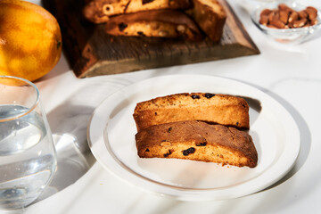 Golden-Brown Almond, Hazelnut and Cranberry Biscotti Slices on Elegant White Plate, Illuminated by Natural Light on Marble Surface