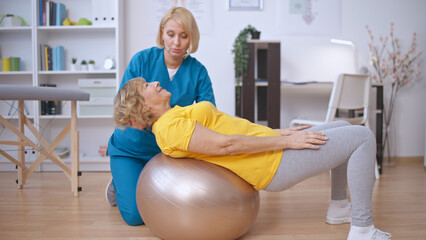 A rehabilitation doctor helps a patient train her back on a fitball, physical medicine