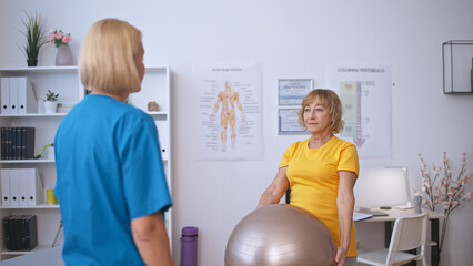 A happy senior woman exercises with a fitball at a rehabilitation center, focusing on recovery