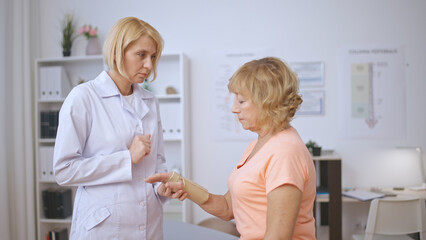 An attentive woman traumatologist examines a female patient's arm in a medical bandage
