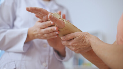 A female traumatologist adjusts a medical band on a mature patient's hand after an examination