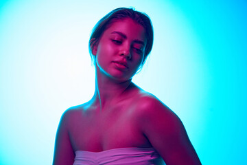 Portrait of tender young beautiful woman in strapless top posing against gradient studio background in neon light. Concept of beauty, skincare, cosmetics and cosmetology