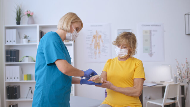 A nurse applies a medical band to a senior patient's injured hand, providing trauma treatment