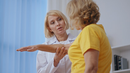 A senior woman undergoes rehabilitation after surgery, attended by a traumatologist