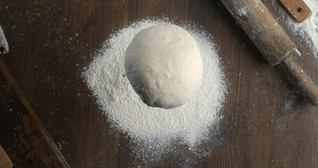 Super slow motion macro of raw loaf of dough falling with flour dust splashes while artisan baker chef making homemade bread, pasta or pizza on rustic wooden table in traditional bakery kitchen.