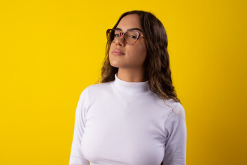 Fototapeta premium Happy young woman wearing glasses and a white blouse, happy on yellow background